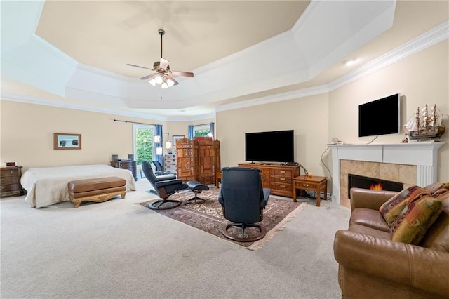 bedroom featuring crown molding, a raised ceiling, carpet flooring, a tile fireplace, and a ceiling fan