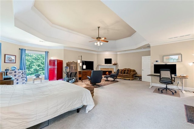 carpeted bedroom with a tray ceiling, ornamental molding, a tile fireplace, and an office area