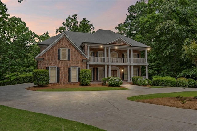 greek revival house with a balcony, curved driveway, a porch, and brick siding
