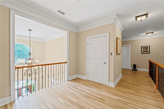 corridor with a chandelier, light wood-style flooring, ornamental molding, and baseboards