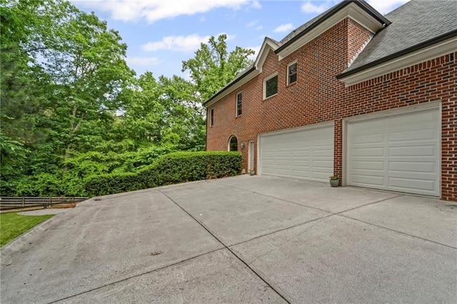 view of side of home featuring brick siding, concrete driveway, fence, and a garage