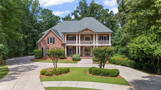neoclassical home featuring a balcony, curved driveway, a front lawn, and covered porch