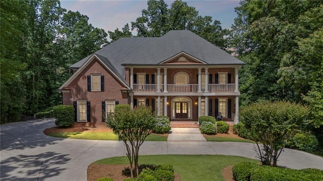 neoclassical / greek revival house featuring a balcony, a porch, curved driveway, and a front lawn