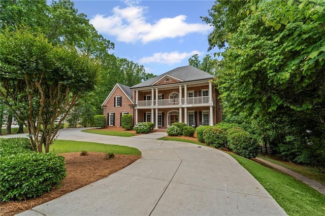 greek revival house featuring a balcony, curved driveway, a porch, and brick siding