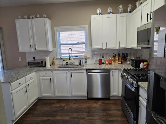 kitchen with a sink, appliances with stainless steel finishes, dark wood-style floors, and white cabinetry