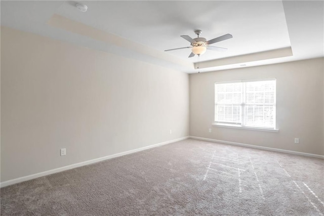 spare room with a raised ceiling, carpet flooring, and ceiling fan