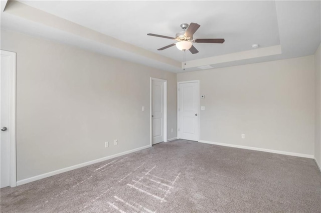 carpeted empty room featuring ceiling fan and a raised ceiling