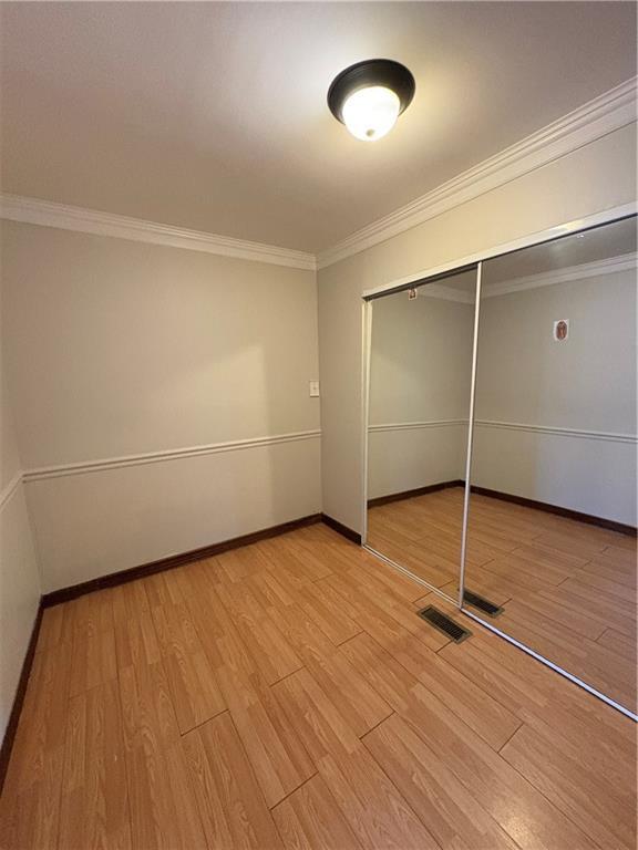 2807 Mcclave Dr, Doraville, GA 30340 - unfurnished bedroom with light wood-style flooring, ornamental molding, a closet, and baseboards