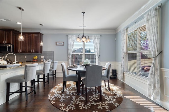 dining space featuring sink, crown molding, dark wood-type flooring, and a chandelier