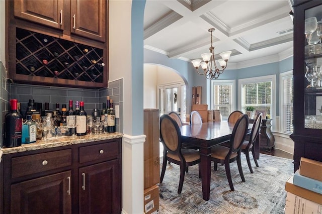 dining area featuring bar, coffered ceiling, a notable chandelier, ornamental molding, and beamed ceiling