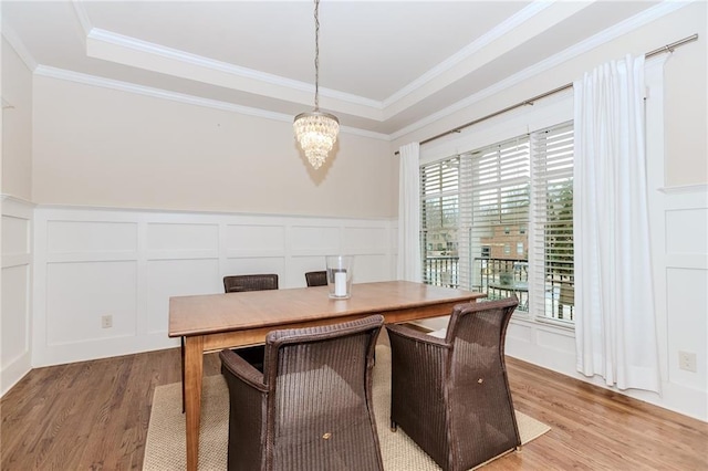 dining room with a decorative wall, light wood-style flooring, plenty of natural light, a chandelier, and wainscoting