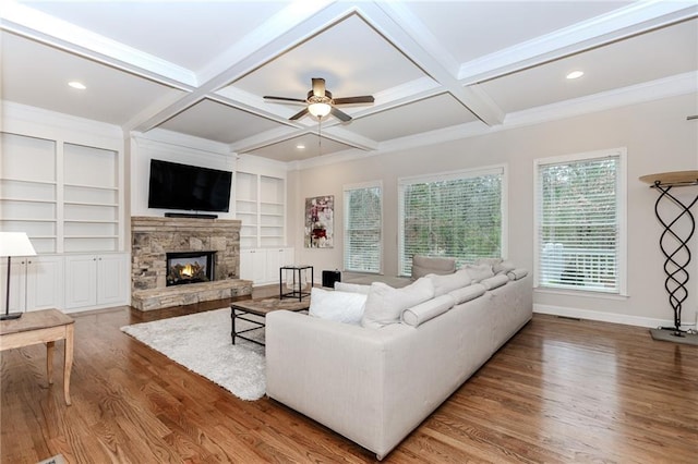 living area featuring wood finished floors, coffered ceiling, ceiling fan, a stone fireplace, and beam ceiling