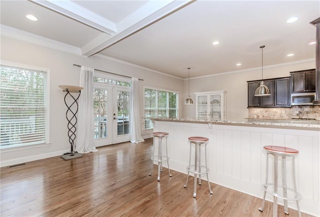 kitchen with a kitchen bar, light wood-type flooring, french doors, dark brown cabinets, and tasteful backsplash