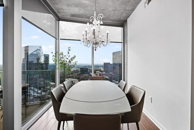 dining room with baseboards, a notable chandelier, wood finished floors, expansive windows, and a view of city