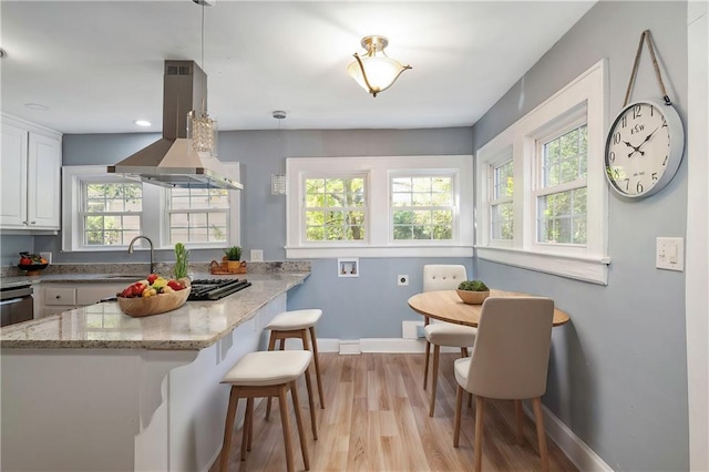 kitchen with hanging light fixtures, light stone countertops, a peninsula, island exhaust hood, and white cabinetry