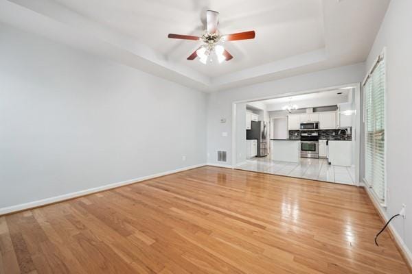 3272 Monarch Pine Dr, Peachtree Corners, GA 30071 - unfurnished living room with light wood-style floors, a tray ceiling, a ceiling fan, and a chandelier