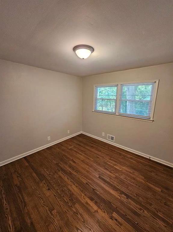 spare room with plenty of natural light, dark wood-style floors, visible vents, and baseboards