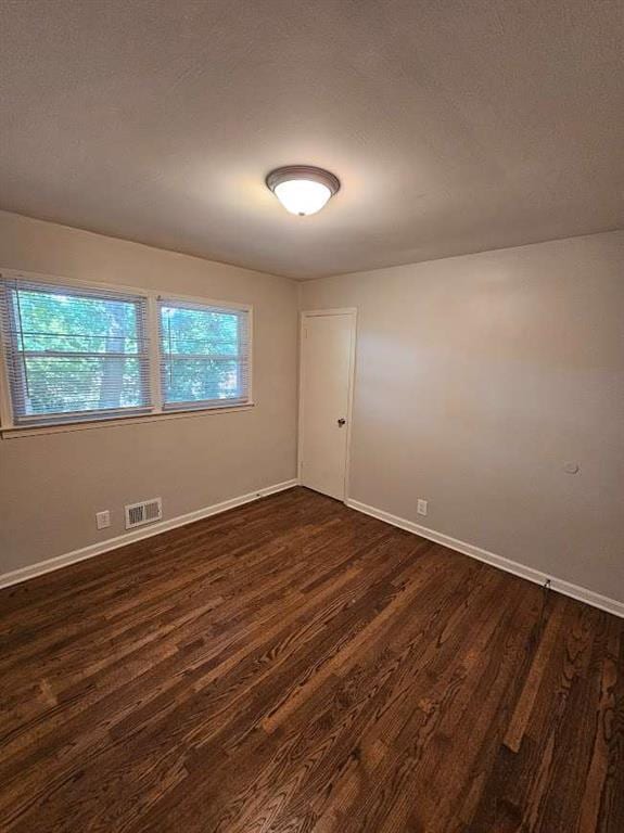 empty room with dark wood-type flooring, a healthy amount of sunlight, visible vents, and baseboards