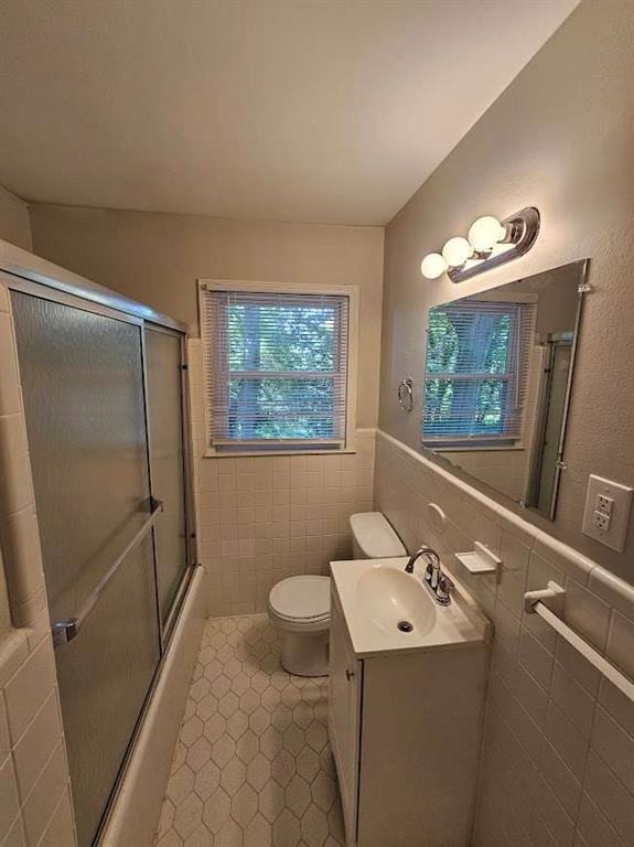 full bath with toilet, vanity, wainscoting, enclosed tub / shower combo, and tile walls