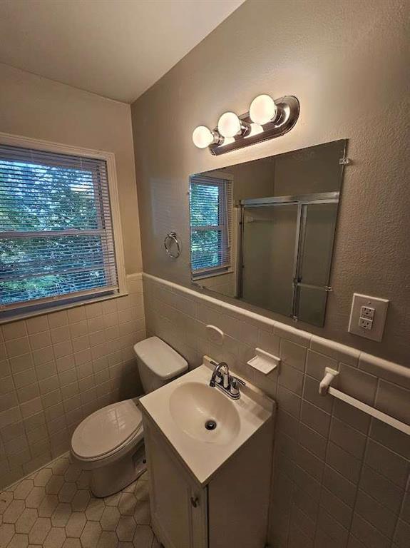 bathroom featuring a wealth of natural light, toilet, tile walls, and a stall shower