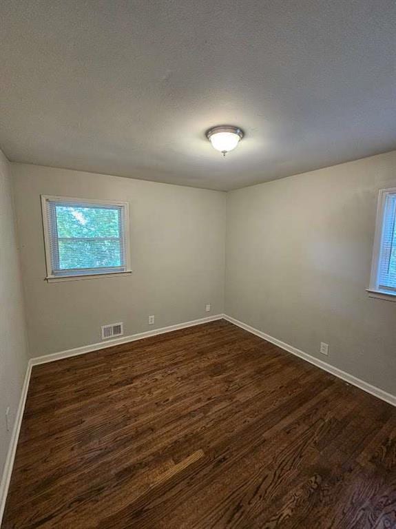 empty room with dark wood finished floors, baseboards, visible vents, and a wealth of natural light