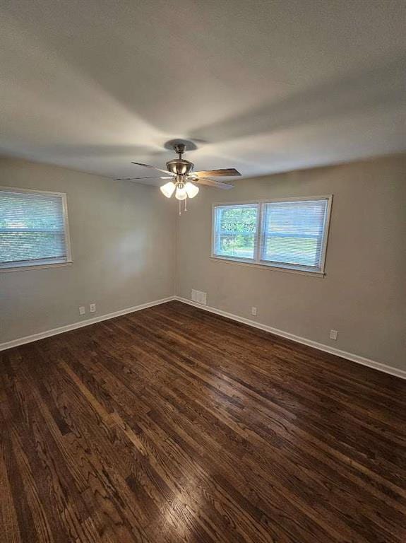 empty room featuring visible vents, dark wood-style floors, baseboards, and ceiling fan