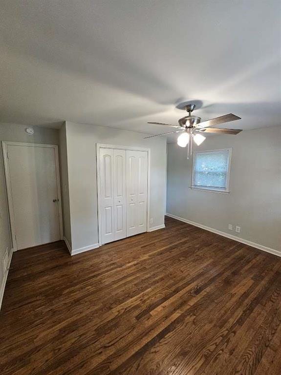 unfurnished bedroom with dark wood-style floors, baseboards, a closet, and ceiling fan