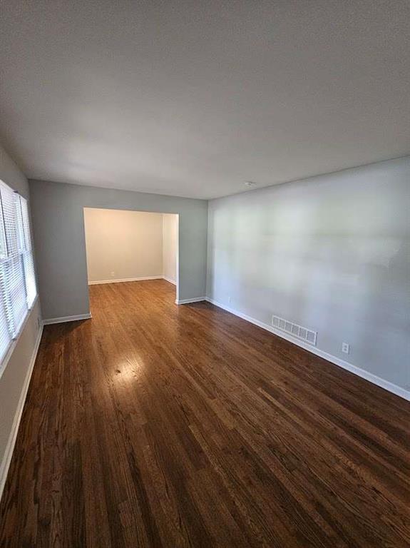 unfurnished room featuring dark wood-style floors, visible vents, and baseboards