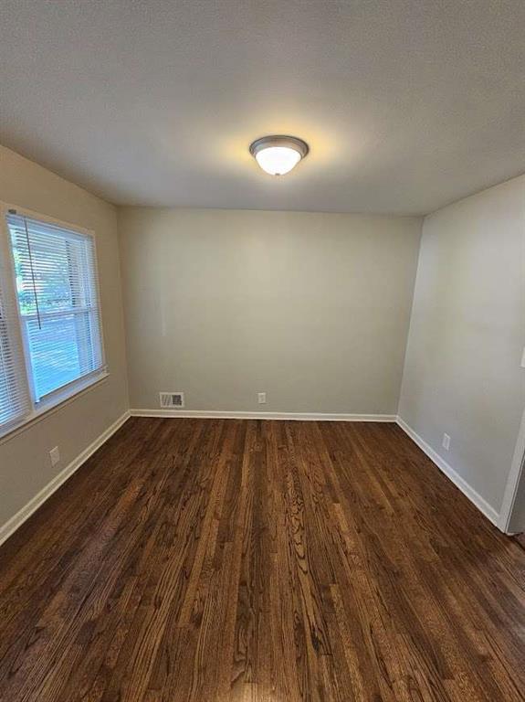 unfurnished room featuring visible vents, baseboards, and dark wood finished floors