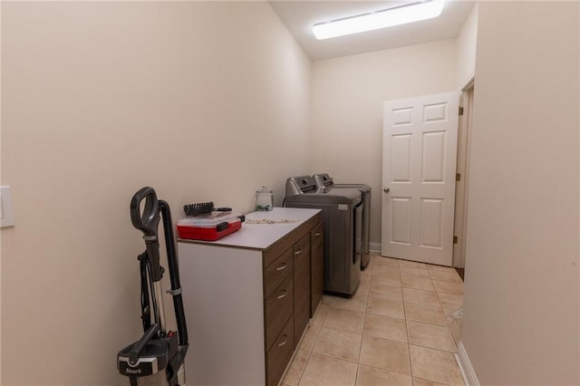 clothes washing area with washing machine and clothes dryer, light tile patterned floors, and cabinets