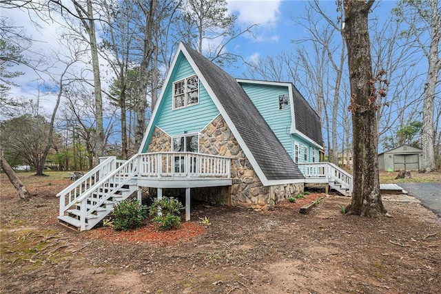 view of front facade with a shingled roof, stone siding, and a wooden deck