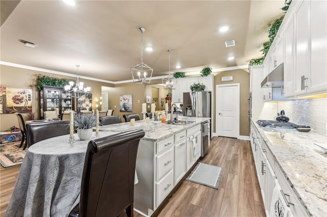 kitchen featuring hanging light fixtures, an island with sink, stainless steel appliances, light stone counters, and white cabinets