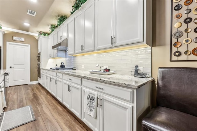 kitchen with light wood-type flooring, stainless steel gas cooktop, light stone countertops, backsplash, and white cabinets