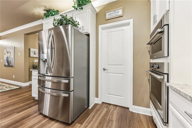 kitchen featuring light wood-type flooring, appliances with stainless steel finishes, white cabinetry, and light stone countertops