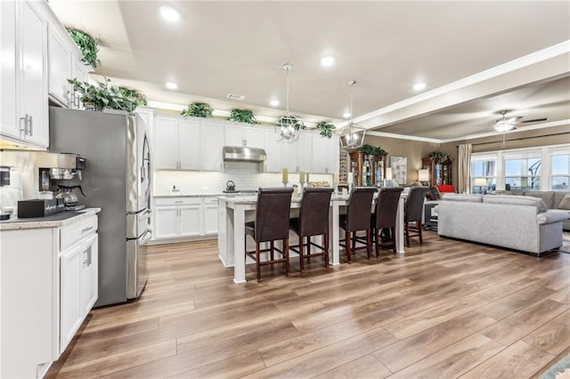 kitchen featuring white cabinetry, a kitchen island with sink, decorative light fixtures, a kitchen breakfast bar, and decorative backsplash