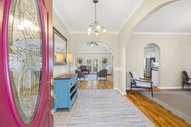 foyer with a notable chandelier, light tile patterned floors, baseboards, arched walkways, and ornamental molding