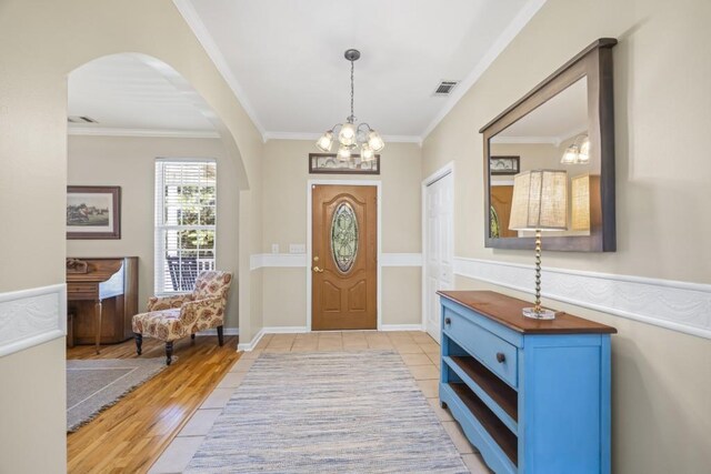 entryway featuring arched walkways, ornamental molding, visible vents, and an inviting chandelier