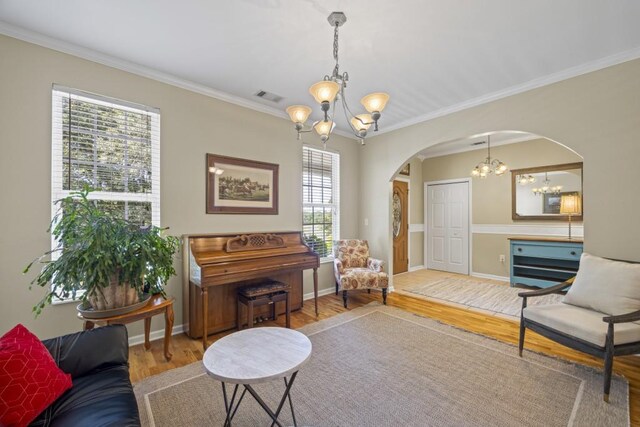 sitting room featuring visible vents, crown molding, wood finished floors, arched walkways, and an inviting chandelier
