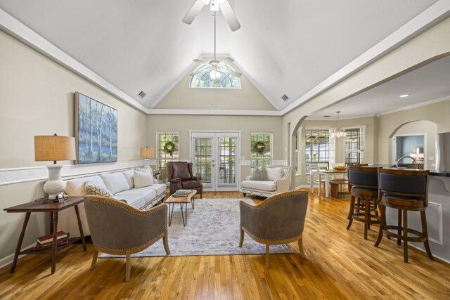 living room with high vaulted ceiling, light wood-type flooring, ceiling fan with notable chandelier, visible vents, and arched walkways