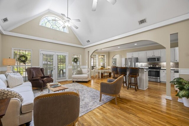 living area featuring arched walkways, light wood-style floors, ceiling fan, and visible vents