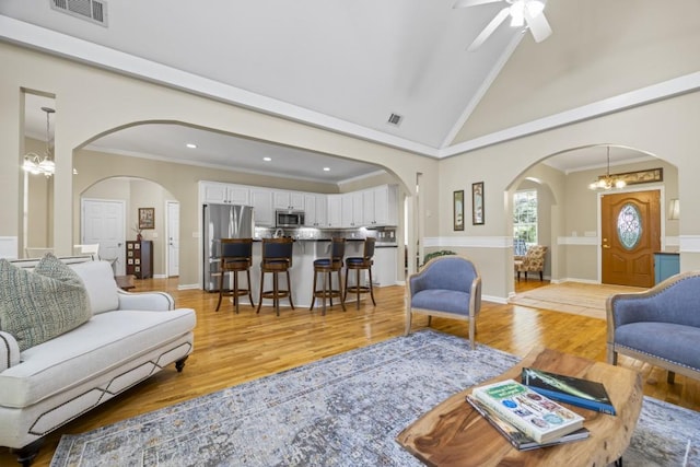 living room featuring lofted ceiling, ceiling fan with notable chandelier, crown molding, and light hardwood / wood-style flooring