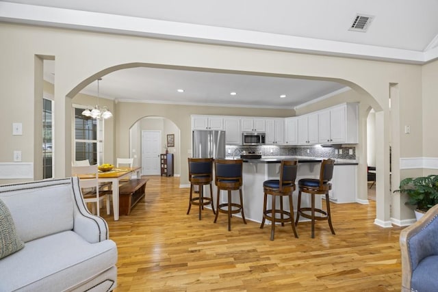 kitchen featuring white cabinets, appliances with stainless steel finishes, hanging light fixtures, and light hardwood / wood-style floors