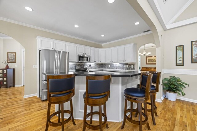 kitchen featuring tasteful backsplash, arched walkways, light wood-style floors, white cabinets, and appliances with stainless steel finishes