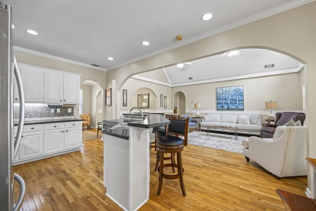 kitchen featuring light wood-type flooring, ornamental molding, stainless steel fridge, a kitchen bar, and white cabinets