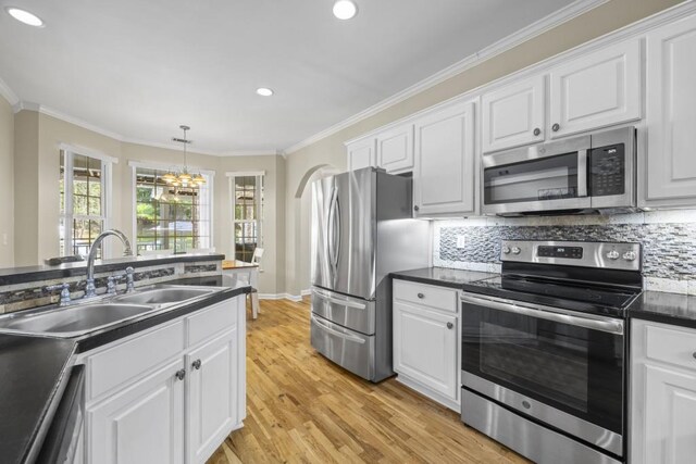 kitchen with a sink, a chandelier, stainless steel appliances, dark countertops, and ornamental molding