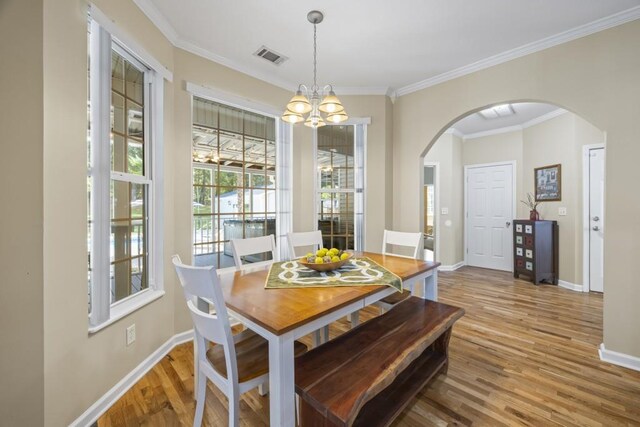 dining room featuring baseboards, ornamental molding, wood finished floors, arched walkways, and an inviting chandelier