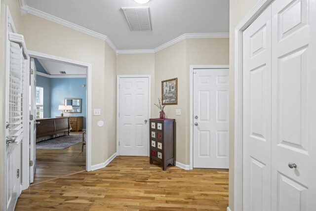 hall with light wood-style flooring, ornamental molding, baseboards, and visible vents