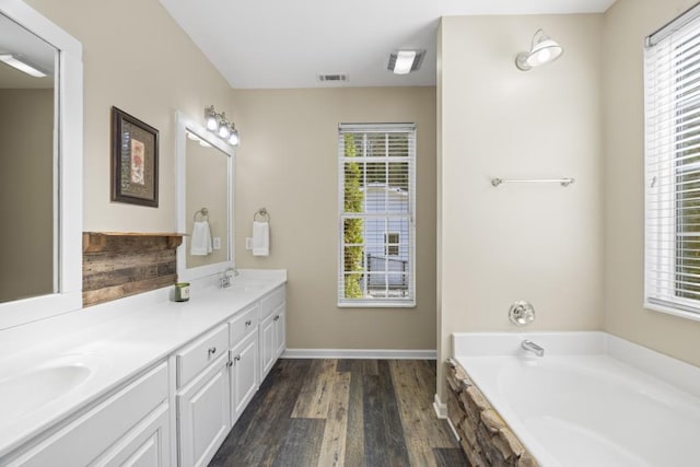 bathroom with a tub to relax in, vanity, and wood-type flooring