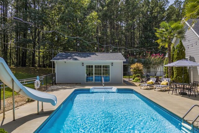 view of pool with a storage structure, a water slide, an outbuilding, fence, and a patio
