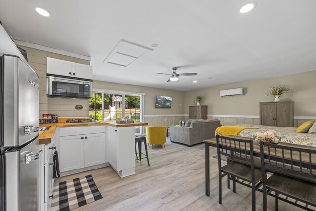 kitchen with open floor plan, butcher block countertops, stainless steel appliances, a wainscoted wall, and a wall mounted air conditioner